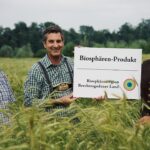 Teilnehmer des Alpenkorn-Projektes halten im Getreidefeld das Biosphären-Produkt-Schild hoch