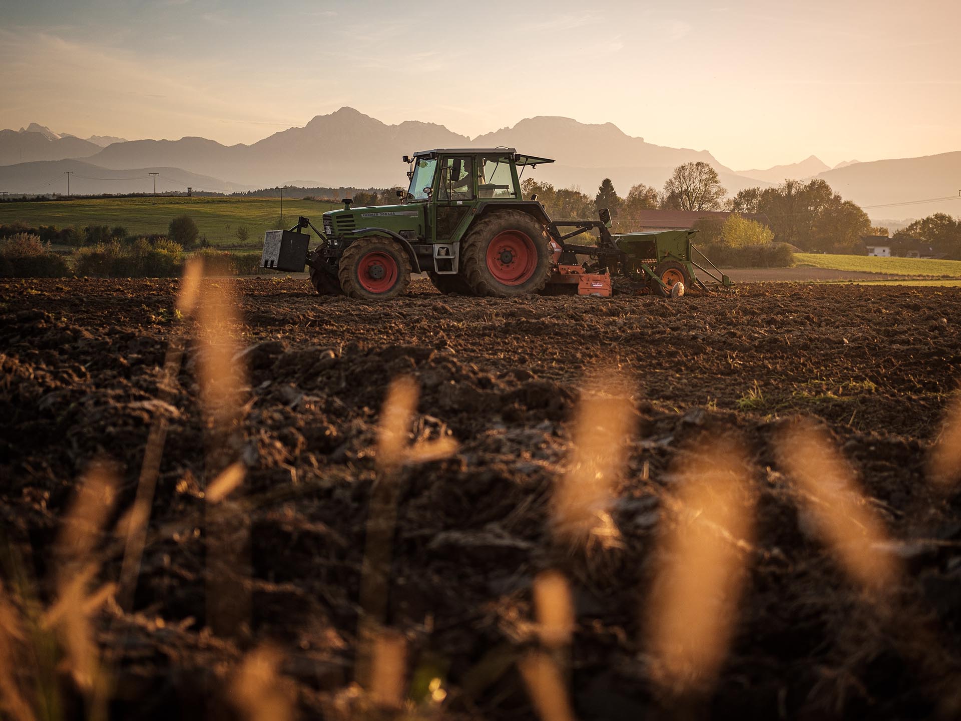 Traktor pflügt vor Bergkulisse einen Acker