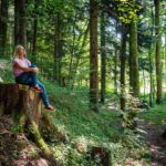 Frau sitzt auf einem Baumstumpf im Wald