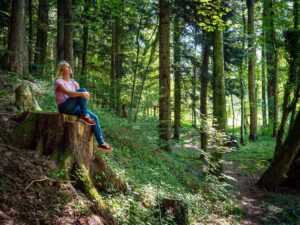 Frau sitzt auf einem Baumstumpf im Wald