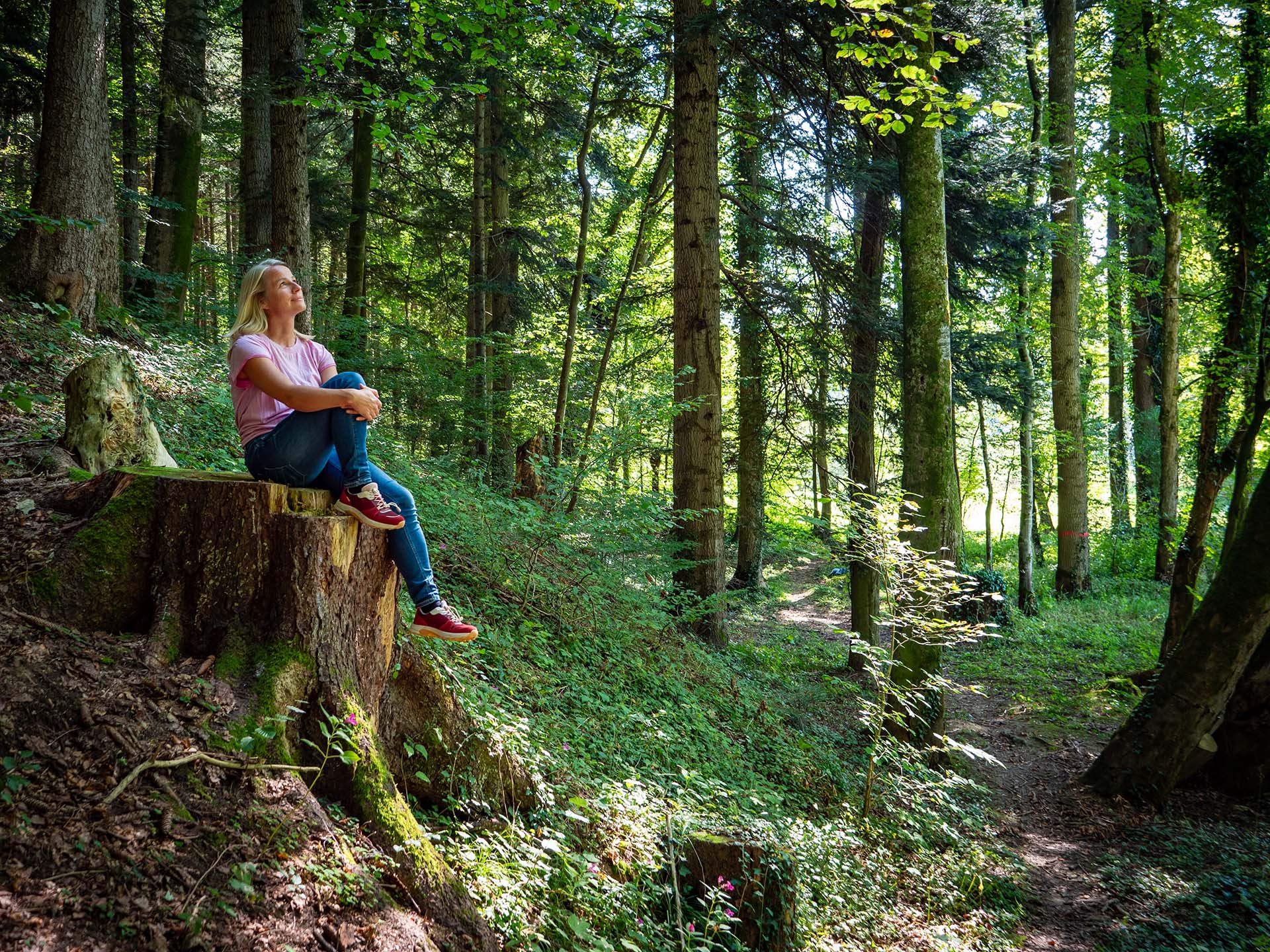 Frau sitzt auf einem Baumstumpf im Wald