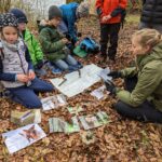 Kinder sitzen am Waldboden und beschäftigen sich mit Bildungsmaterial zu Tieren im Wald