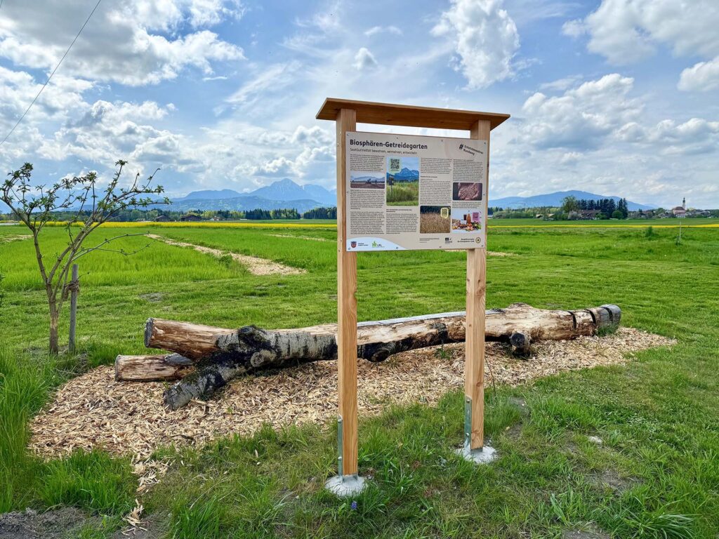 Infotafel am Biosphären-Getreidegarten mit Bergkulisse im Hintergrund
