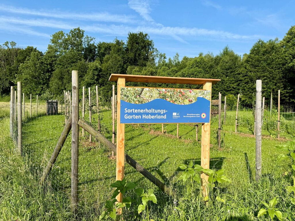 Schild am Sortenerhaltungsgarten Haberland mit Obstbäumen im Hintergrund