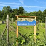 Schild am Sortenerhaltungsgarten Haberland mit Obstbäumen im Hintergrund