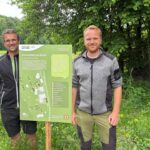 Hans Lecker vom Biohof Lecker und Luis Frank von der Biosphären-Verwaltungsstelle mit einem Schild zum Thema "Wilde Ecken"