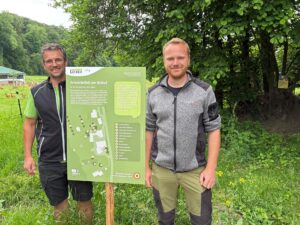 Hans Lecker vom Biohof Lecker und Luis Frank von der Biosphären-Verwaltungsstelle mit einem Schild zum Thema "Wilde Ecken"